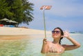 Young pretty and sweet Chinese Asian woman on the beach taking selfie picture portrait with mobile phone camera enjoying holiday h Royalty Free Stock Photo