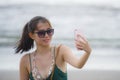 Young pretty and sweet Chinese Asian woman on the beach taking selfie picture portrait with mobile phone camera enjoying holiday h Royalty Free Stock Photo