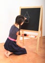 Girl drawing house on black blackboard