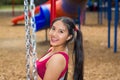 Young pretty teenage girl with pig tails wearing jeans and purple top, sitting on swing at outdoors playground, smiling Royalty Free Stock Photo