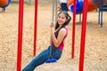 Young pretty teenage girl with pig tails wearing jeans and purple top, sitting on swing at outdoors playground, smiling Royalty Free Stock Photo