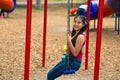 Young pretty teenage girl with pig tails wearing jeans and purple top, sitting on swing at outdoors playground, smiling Royalty Free Stock Photo