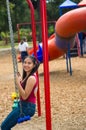 Young pretty teenage girl with pig tails wearing jeans and purple top, sitting on swing at outdoors playground, smiling Royalty Free Stock Photo