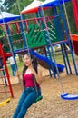 Young pretty teenage girl with pig tails wearing jeans and purple top, sitting on swing at outdoors playground, smiling Royalty Free Stock Photo