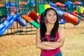 Young pretty teenage girl with pig tails wearing jeans and purple top, standing in front of outdoors playground, smiling Royalty Free Stock Photo