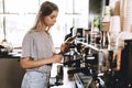 A young pretty thin blonde,dressed in casual outfit,is cooking coffee in a popular coffee shop.