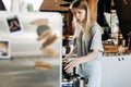 A young pretty thin blonde,dressed in casual outfit,is cooking coffee in a popular coffee shop.