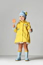 Young pretty toddler girl kid with big sweet lollypop candy in yellow jacket and rubber boots