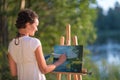 Young pretty woman artist draws paints a picture of lake on open plain air outdoors