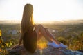 Young pretty woman in black short summer dress sitting on a rock relaxing outdoors at sunset. Fashionable female enjoying warm Royalty Free Stock Photo