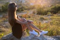 Young pretty woman in black short summer dress sitting on a rock relaxing outdoors at sunset. Fashionable female enjoying warm Royalty Free Stock Photo