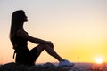 Young pretty woman in black short summer dress sitting on a rock relaxing outdoors at sunset. Fashionable female enjoying warm Royalty Free Stock Photo