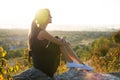 Young pretty woman in black short summer dress sitting on a rock relaxing outdoors at sunset. Fashionable female enjoying warm Royalty Free Stock Photo