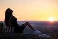 Young pretty woman in black short summer dress sitting on a rock relaxing outdoors at sunset. Fashionable female Royalty Free Stock Photo