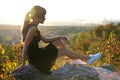 Young pretty woman in black short summer dress sitting on a rock relaxing outdoors at sunset. Fashionable female Royalty Free Stock Photo