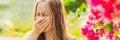 Young pretty woman blowing nose in front of blooming tree. Spring allergy concept BANNER, LONG FORMAT