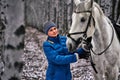 Young pretty woman in a blue jacket and a sports hat for a walk with a white horse Royalty Free Stock Photo