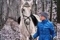 Young pretty woman in a blue jacket and a sports hat for a walk with a white horse Royalty Free Stock Photo