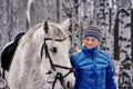 Young pretty woman in a blue jacket and a sports hat for a walk with a white horse Royalty Free Stock Photo