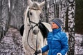 Young pretty woman in a blue jacket and a sports hat for a walk with a white horse Royalty Free Stock Photo