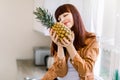Young pretty woman in casual shirt enjoying her breakfast or lunch with fresh fruits, smelling pineapple with eyes