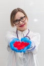 Young pretty woman doctor in a white medical coat and rubber gloves with a phonendoscope holds a red heart in her hands in a hospi Royalty Free Stock Photo