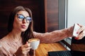 Young pretty woman freelancer makes a selfie and enjoys coffee in the cafe Royalty Free Stock Photo