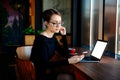 Young pretty woman in glasses works on a laptop, uses a smartphone, a freelancer, a computer, financial analyst, a sales manager. Royalty Free Stock Photo