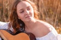 Young pretty woman with long hair musician playing acoustic guitar at sunset field Royalty Free Stock Photo