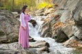 Young pretty woman in long pink fashionable dress standing near small river with fast moving water Royalty Free Stock Photo