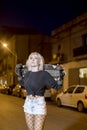 Front view of young pretty woman looking camera in shorts while standing on the street holding a skateboard at night in the city Royalty Free Stock Photo