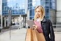 Young pretty woman with paper bags after shopping, holding a tablet in her hands and walking around the city Royalty Free Stock Photo