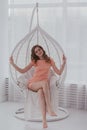 A young woman in a pink dress sitting in a white hanging chair and smiling Royalty Free Stock Photo
