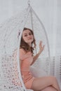 A young woman in a pink dress sitting in a white hanging chair Royalty Free Stock Photo