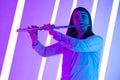 Young pretty woman plays the flute. Musician female posing in a dark studio against the backdrop of bright neon lights