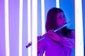 Young pretty woman plays the flute. Musician female posing in a dark studio against the backdrop of bright neon lights