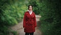 Young pretty woman in red coat looks at camera at blurred spring green park or forest background Royalty Free Stock Photo