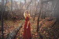 Young pretty woman in the red dress is walking in the foggy mystical forest