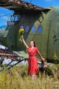 Young woman in a red pin up dress waves a bunch of yellow wildflowers at an abandoned airplane Royalty Free Stock Photo