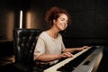 Young pretty woman sensually playing on electric piano and singing a song in recording studio. Attractive musician