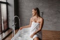 Young pretty woman sitting on bathtub and filling it with water and bubbles, checking water temperature and smiling Royalty Free Stock Photo