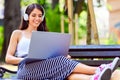 Beautiful young woman sitting on bench in the park, using laptop computer Royalty Free Stock Photo