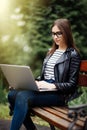 Young pretty woman sitting on bench in the park, using laptop computer, networking online on wireless. Student work on laptop in p Royalty Free Stock Photo