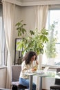 Young pretty woman sitting at cozy home holding phone using laptop. Royalty Free Stock Photo