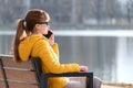 Young pretty woman sitting on a park bench talking on her smartphone outdoors in warm autumn evening Royalty Free Stock Photo