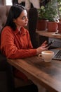 Young pretty woman sitting at table holding smartphone and using laptop computer, looking at mobile phone while remote Royalty Free Stock Photo