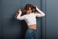 Young pretty woman in stylish casual wear straightens hair and looks down near a wooden wall in the studio. Cute red-haired girl Royalty Free Stock Photo