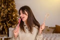 Young pretty woman in sweater, dark hair laughing with red white candy canes, against background of bed, Christmas tree Royalty Free Stock Photo
