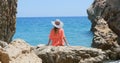 Young pretty woman in swimsuit and coverup sitting on the rocks near the sea