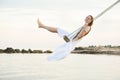 Young pretty woman swinging on a rope swing tied to a tree above the water. Summer vacation. Harmony